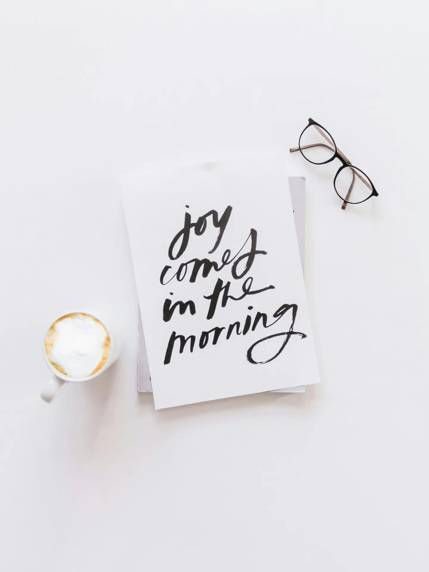 brown framed eyeglasses,latte, and joy comes in the morning note on white surface